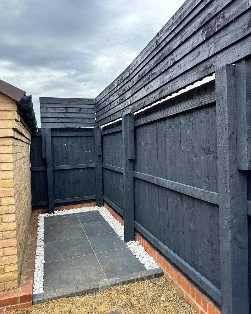 Garden fencing, posts and rails sprayed dark grey, cut in against the brickwork