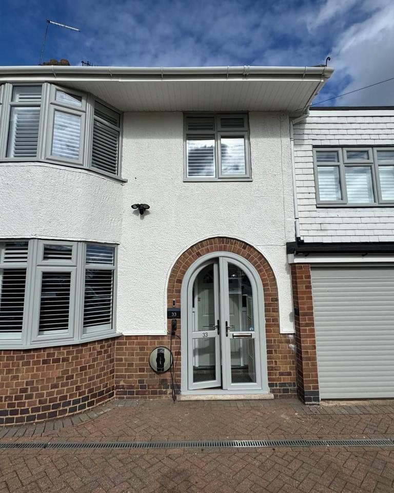 Two bay windows, an arched front door and a garage door sprayed in a soft sage grey