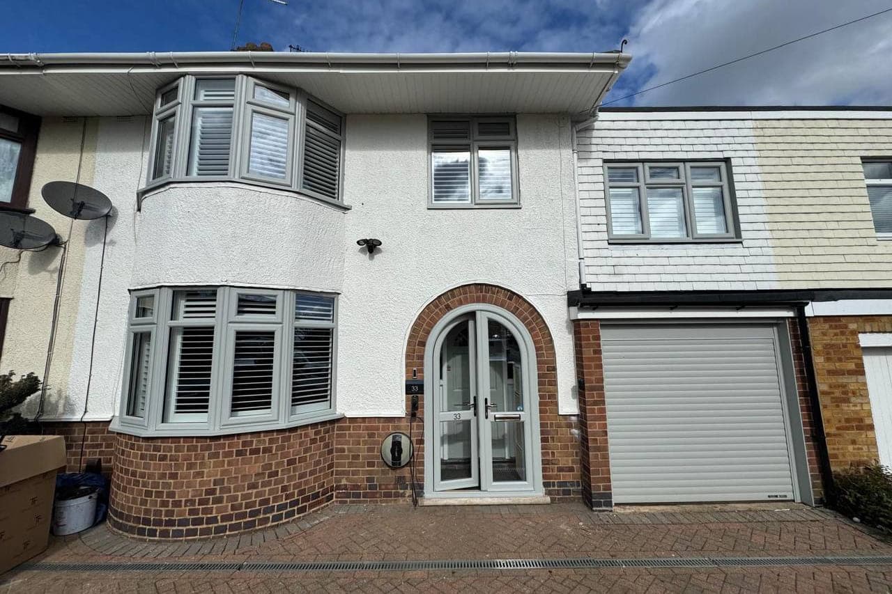 Two bay windows, an arched front door and a garage door sprayed in a soft sage grey