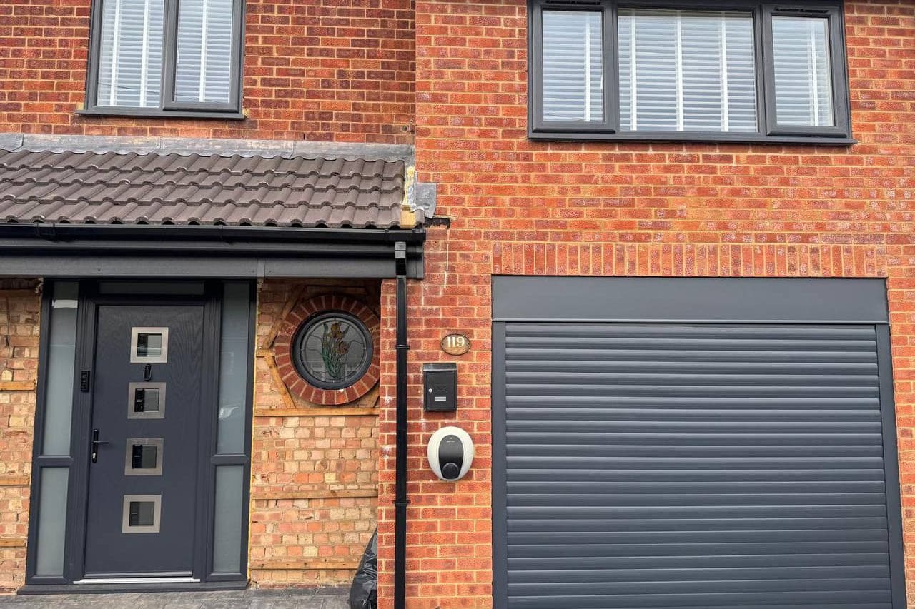 An anthracite roller garage door, front door and windows on one elevation