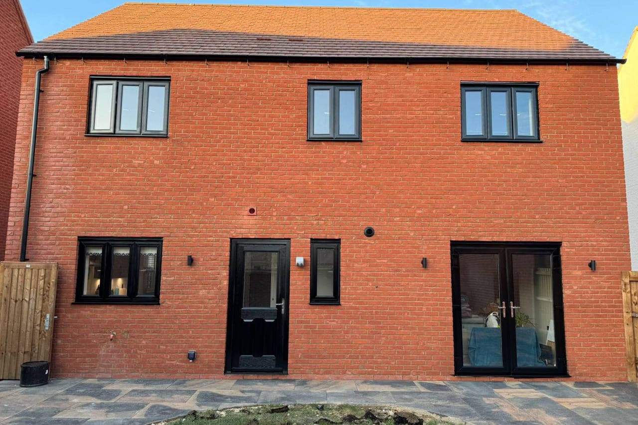 Black sprayed windows, French doors and a front door across a new build elevation